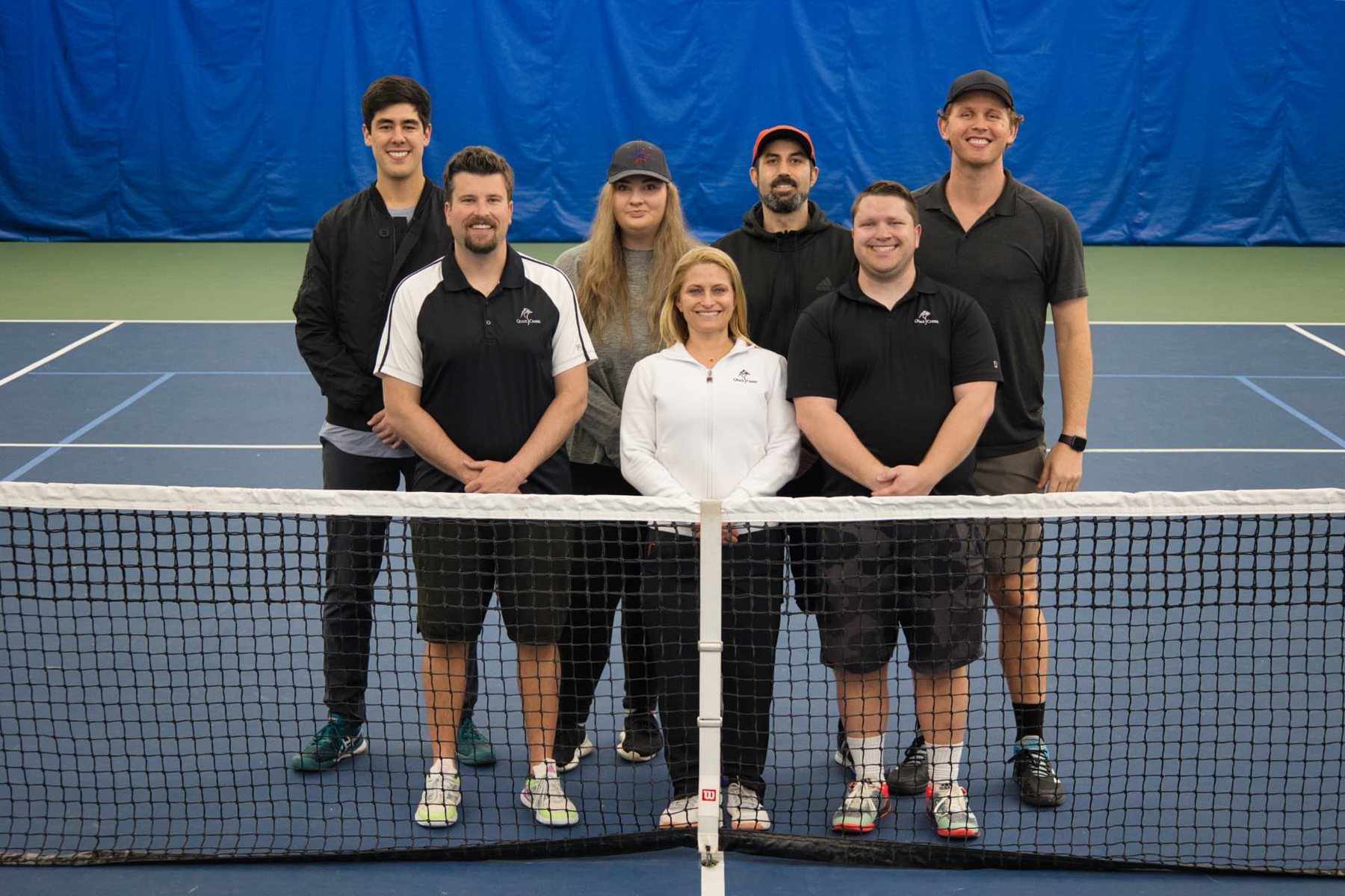 Caleb Bow with a tennis teaching team at the net of an indoor court